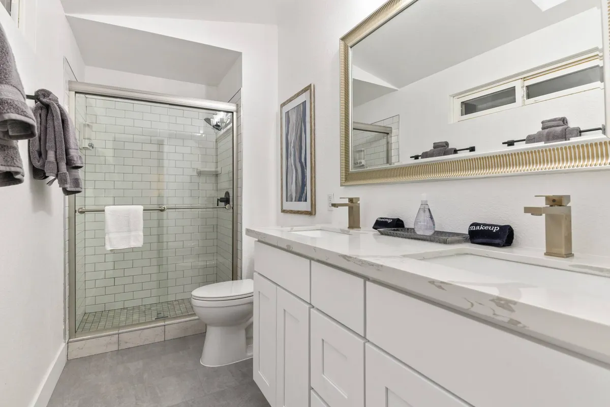 A modern bathroom with a double sink vanity, a large framed mirror, a glass shower stall, and white subway tile walls. The space looks fresh, functional, and inviting, providing a perfect spot for self-care and relaxation.
