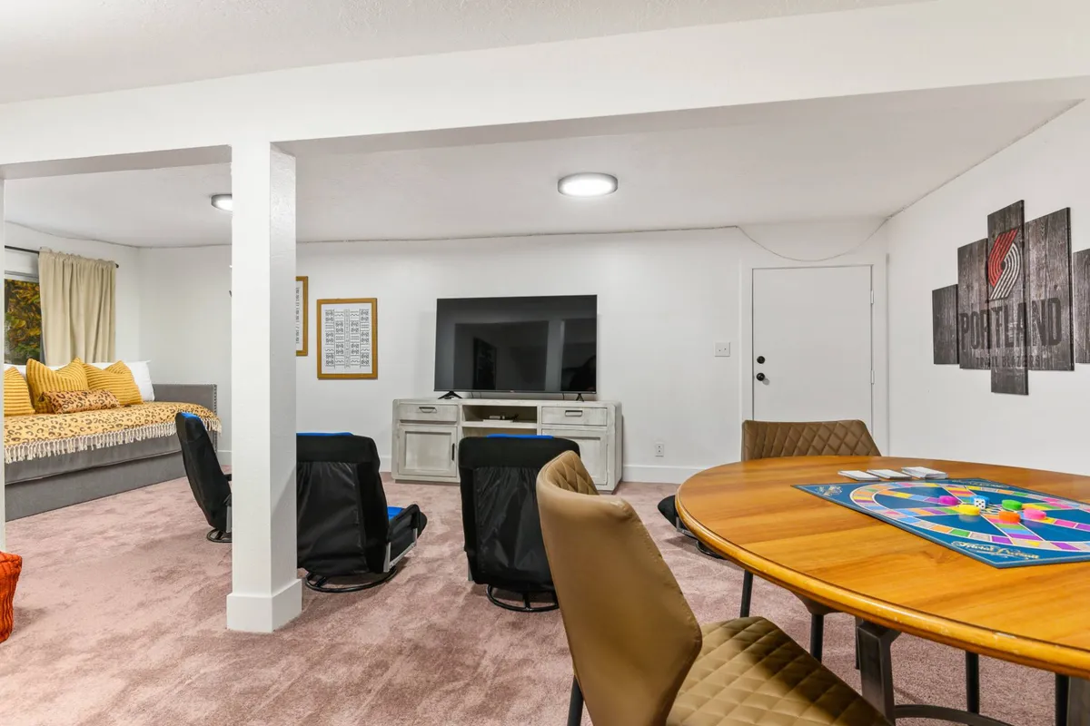 A comfortable and inviting entertainment room with a large TV, a spacious gray sofa, and a dining table set up with a board game. The room is brightly lit, creating a fun, relaxed environment perfect for movie nights and family game sessions.