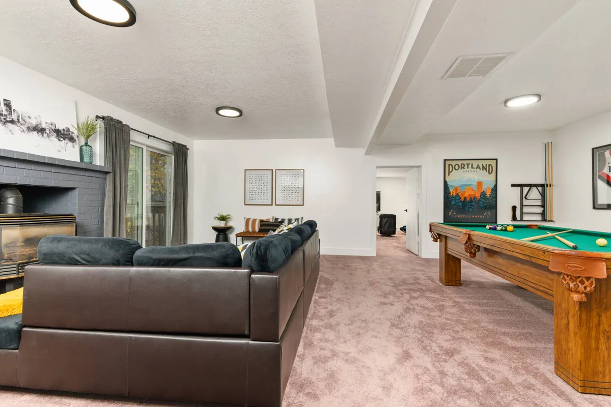 An inviting interior scene with a plush sofa, a pool table, and a glowing fireplace, set against tasteful artwork. The setup encourages friendly competition, relaxation, and group entertainment, capturing the energy of game nights and social gatherings.