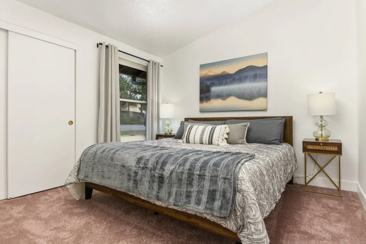 A serene bedroom featuring a comfortable bed adorned with soft bedding, complemented by stylish artwork on the walls, matching nightstands, and neutral curtains. The overall atmosphere is peaceful and inviting, ideal for unwinding at the end of the day.