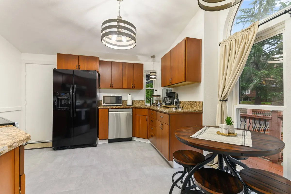 An inviting kitchen scene featuring elegant cabinetry, a stylish black refrigerator, a circular dining table, and a window streaming in natural light. The setting is perfect for casual meals, baking sessions, and intimate family celebrations, reflecting the warmth and functionality of the eat-in bar and dining area.