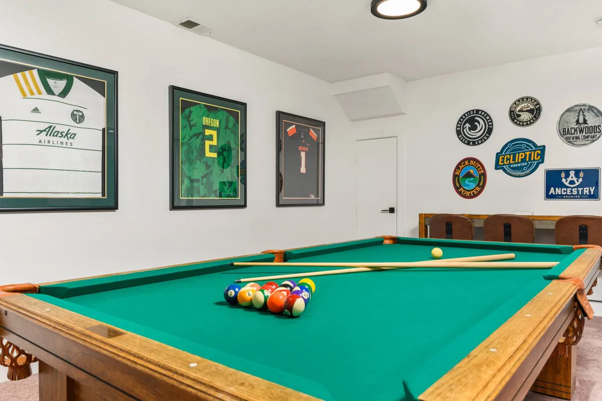 The hero image showcases a stylish game room featuring a full-size pool table, vibrant framed sports jerseys on the walls, and tasteful decorative art, creating an inviting space for relaxation and entertainment. The room is designed for socializing, with ample space for guests to gather, play games, and enjoy each other's company.