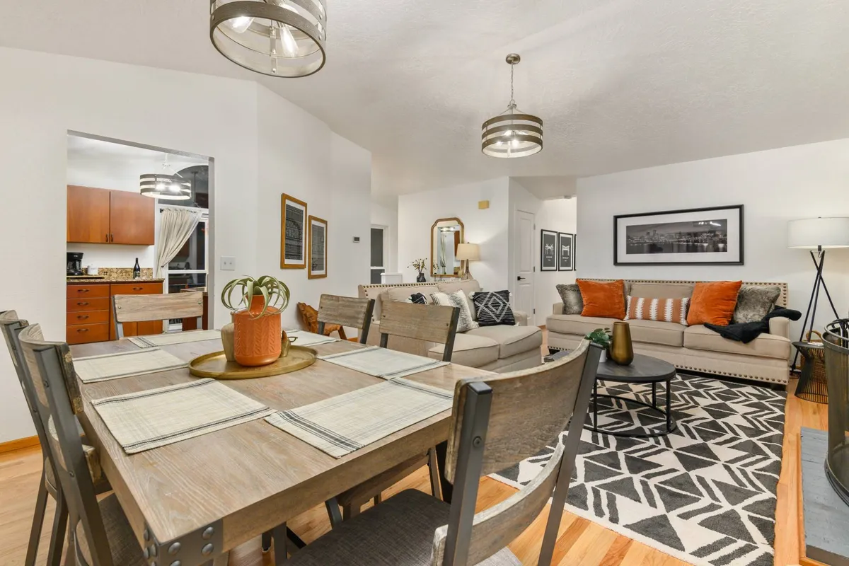 A cozy, well-appointed space that combines a dining table with elegant place settings, a comfortable sofa with decorative pillows, tasteful artwork, and chic lighting. The arrangement encourages lingering conversations and special gatherings, all with a welcoming, communal feel.