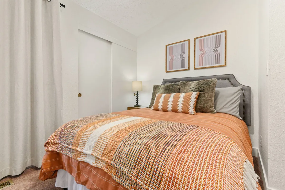 A cozy bedroom with a striking orange knit blanket and decorative pillows on the bed, complemented by contemporary wall art. The space feels warm, welcoming, and designed for comfort and relaxation, ideal for guests seeking privacy and rest.