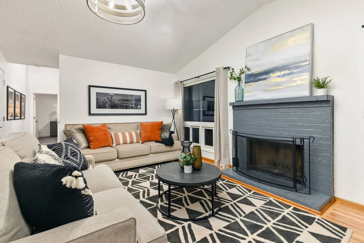 A spacious living area featuring a comfortable sofa with orange cushions, a cozy fireplace, and a coffee table arranged for group relaxation or collaborative activities. The room exudes warmth and invites conversation or brainstorming sessions.